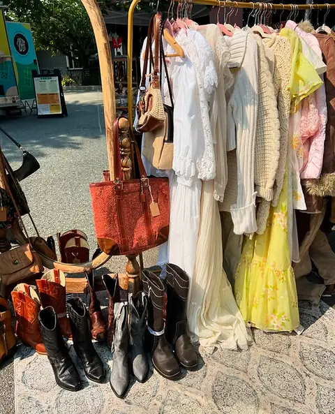 A rack of clothing, bags, and boots displayed outdoors.