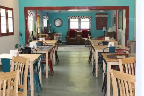 An interior view of a dining room with multiple wooden tables and chairs leading to a living area.