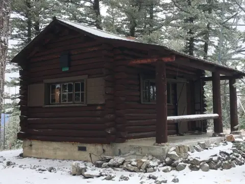 A rustic log cabin stands in a snowy forest.
