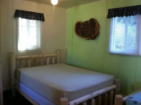 A bedroom with a rustic wooden bed frame and two windows.
