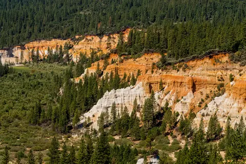 A landscape shows a forested valley with exposed red and white cliffs.