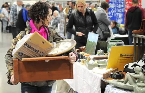 A woman carries a wooden box and a clock while shopping at an indoor market.