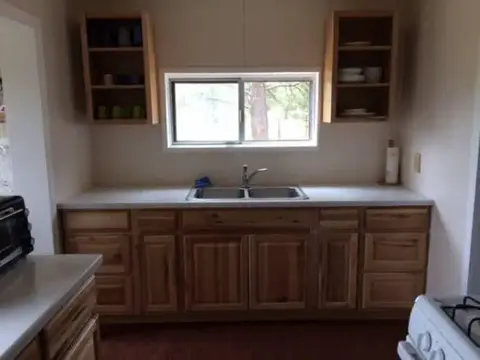 A kitchen interior with wooden cabinets and a double sink below a window.