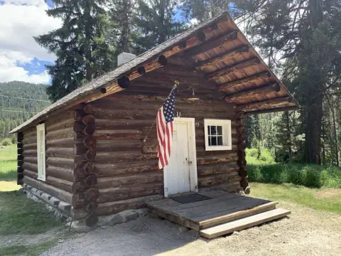 A rustic log cabin with an American flag mounted near the front door.