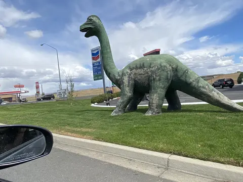 A large green dinosaur statue stands on a grassy area outdoors.