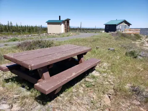 A picnic table sits in a grassy clearing with small cabins in the background.