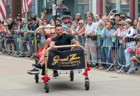 People riding in a decorated luggage cart during an outdoor event with a crowd watching.