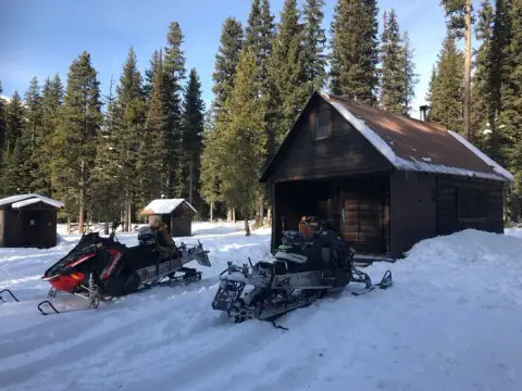 Snowmobiles parked outside a rustic cabin in a snowy forest.