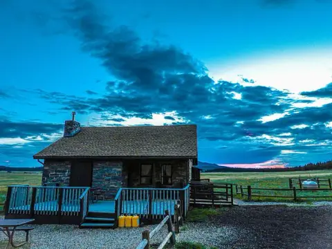An exterior view of a stone cabin with a wooden deck under a dramatic cloudy sky.