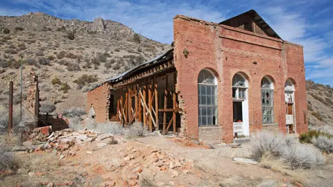 An old brick building ruin with arched windows stands in a desert landscape.