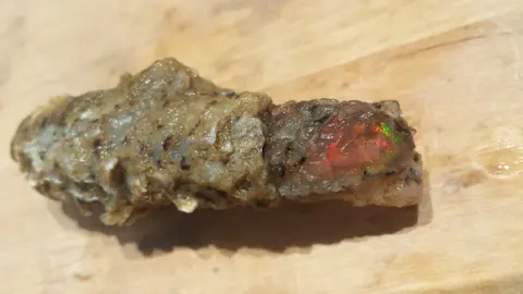 A rough opal specimen on a wooden surface.