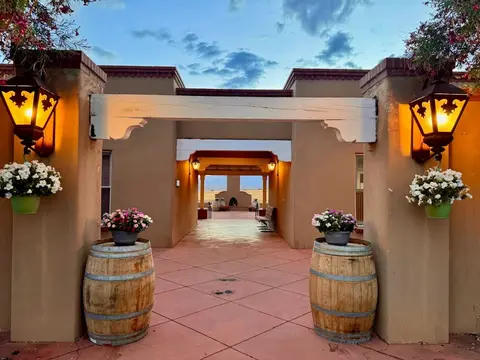 An outdoor pathway framed by pillars, lanterns, flower pots, and wine barrels leading to a distant view.