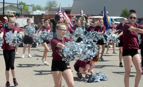 A group of cheerleaders in matching shirts and pom-poms perform in a parade.