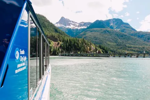 A view of a blue boat on the water with mountains in the background.
