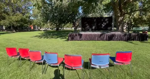 An outdoor stage set up in a grassy park with rows of chairs facing it.