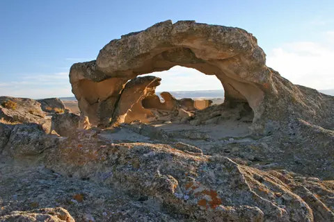 A natural rock arch formation in a desert landscape under a clear sky.