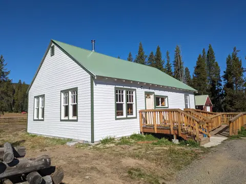 A white building with a green roof and a wooden deck sits outdoors.