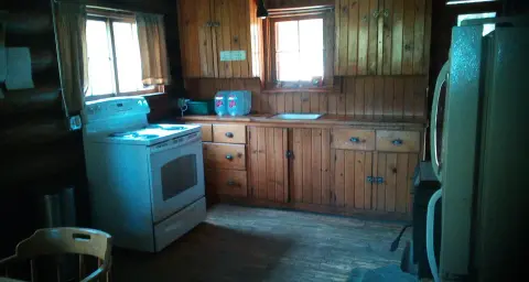A rustic kitchen interior with wood paneling, a white stove, and cabinets.