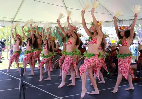 A group of dancers perform on a stage under a white canopy.