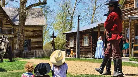 People in historical costumes stand outdoors in a village.