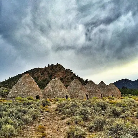 A row of stone beehive-shaped kilns stands in a landscape under a cloudy sky.