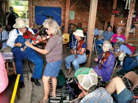 Several musicians play fiddles indoors while an audience watches.