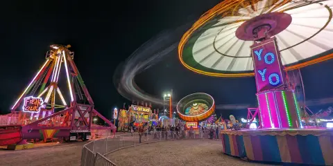 Brightly lit amusement park rides operate at a carnival at night.