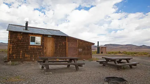 A rustic wooden cabin with picnic tables outside under a cloudy sky.
