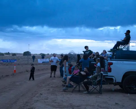 A group of people gathered outdoors near parked trucks at dusk.