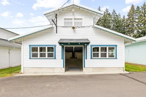 Exterior view of a white wooden building with blue-trimmed windows and an open doorway.