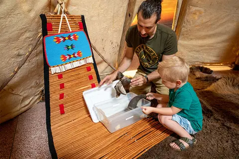 A man and a child look at horns inside a tipi.