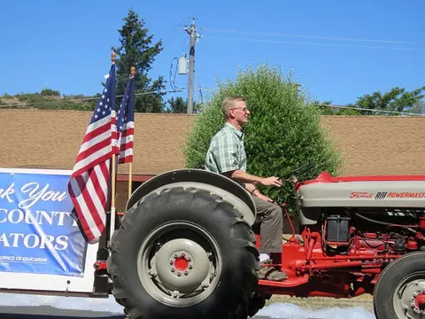 A man drives a red tractor with American flags attached to it.