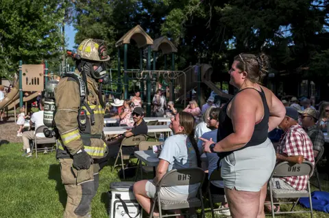 A firefighter in full gear speaks with attendees at an outdoor gathering near a playground.