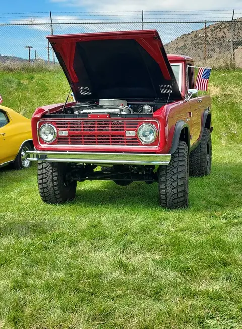 A red vintage truck is parked on a grassy field with its hood open.