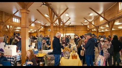 A large crowd gathers inside a rustic wooden hall for an event or market.