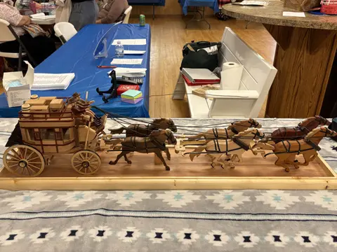 A detailed wooden model of a stagecoach with horses sits on a table indoors.
