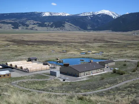 An elevated wide-angle view of a fish hatchery facility situated in a wide valley with snow-capped mountains in the background.