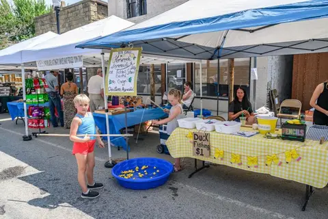 A child plays a duck fishing game at an outdoor street market booth.