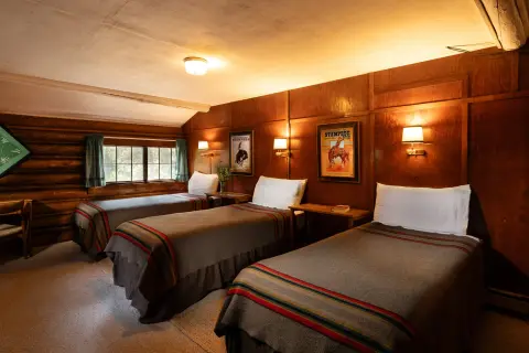 A rustic bedroom with three single beds and wood paneled walls.
