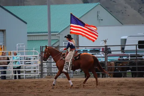 A woman riding a horse carries an American flag at a rodeo.