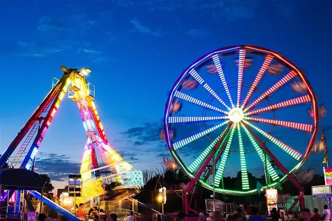 A brightly lit carnival ride and Ferris wheel at night.