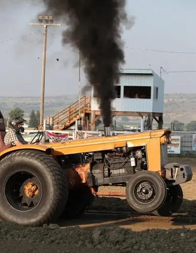 A tractor pulls a load while emitting thick black smoke during a tractor pull event.