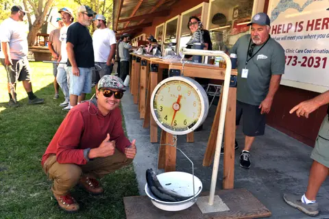 A man crouches next to a scale weighing a fish while others look on.