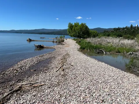 A pebbled shoreline along a lake under a clear blue sky.
