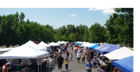 People walk among vendor tents at an outdoor market.