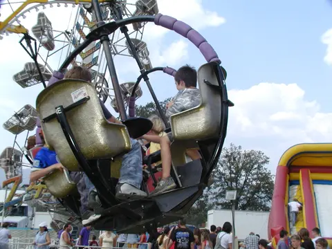 People ride a carnival attraction with a crowd below.