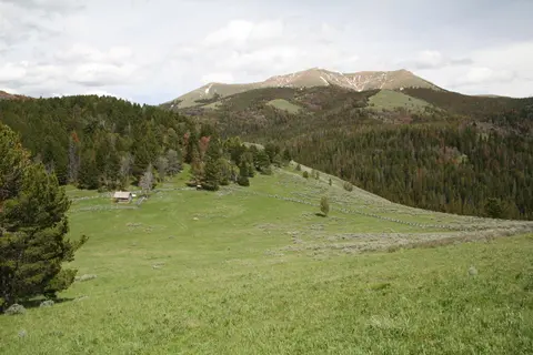 A scenic view of a green mountain landscape with a small cabin and distant peaks.