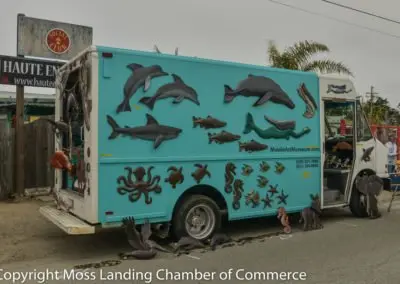 A light blue and white delivery truck decorated with metal marine animal sculptures.