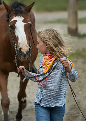 A young girl leads a horse by its reins.