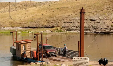 A car and a person on a cable ferry crossing a river.
